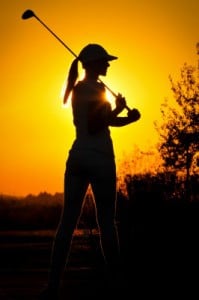 Woman playing golf at sunset.